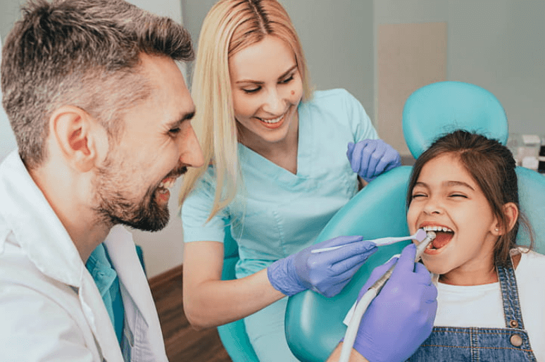 dentist and his dental assistant cleaning a young girls teeth who is smiling