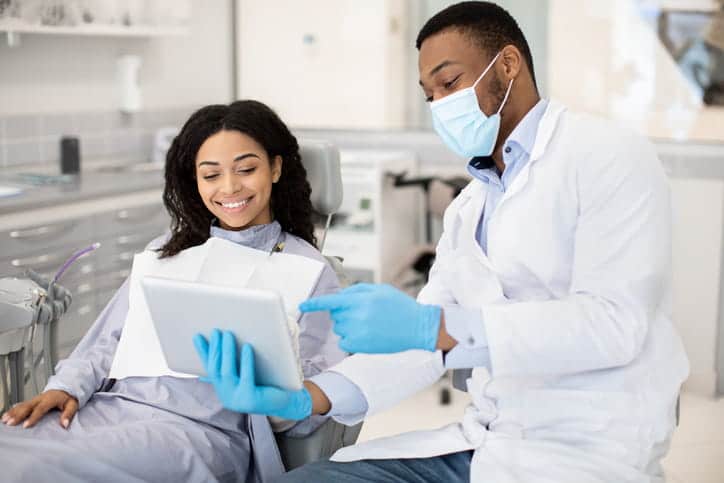 A male dentist showing his female patient her medical records. She is smiling, sitting in the dentist chair.