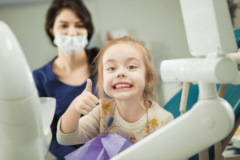 a young girl at the dentists office giving a thumbs up