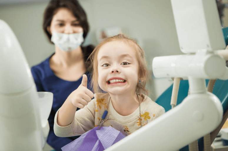 A young girl at the dentists office giving a thumbs up