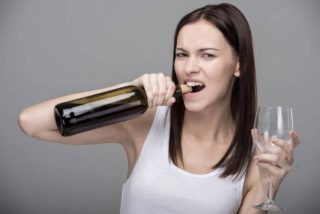 Woman using teeth to open wine bottle