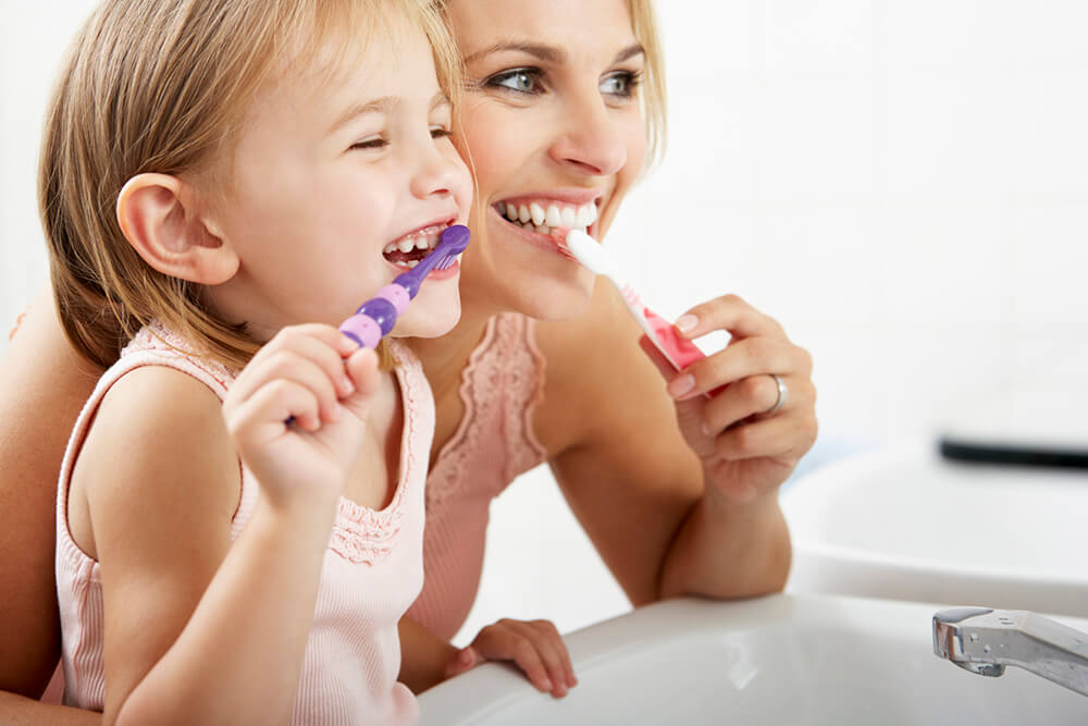 Mom showing daughter how to brush teeth