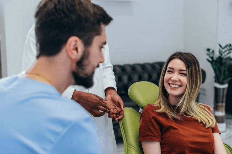 a male dentist is speaking with his female client who is smiling in a dentist's chair.