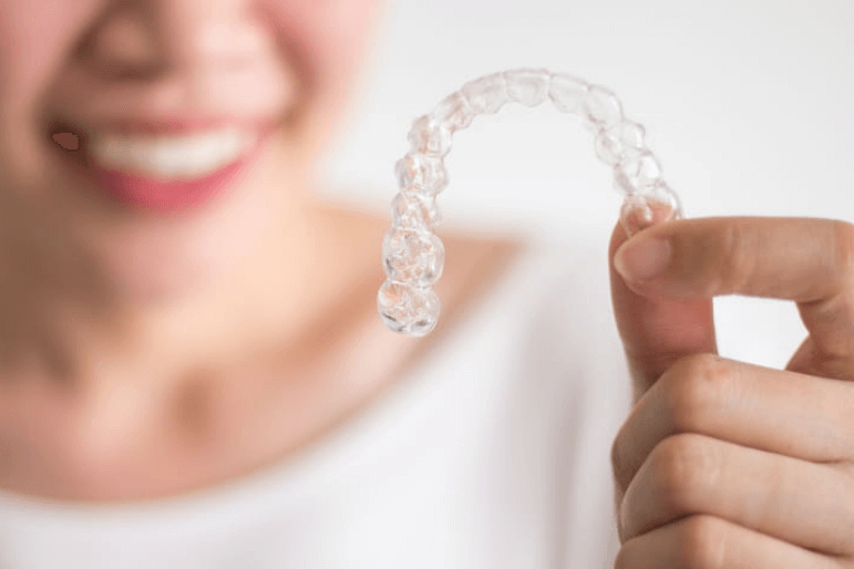 Focus is on invisalign, which a woman holds in her hand up to the camera. She is blurred out in the background.