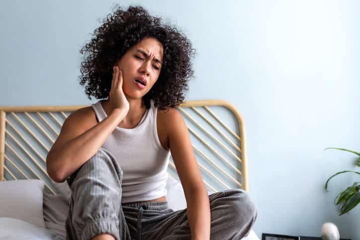 A woman holding her face in pain due to a dental emergency. 