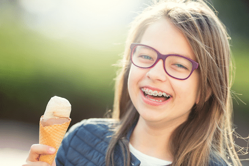 A little girl with braces is smiling and holding an ice cream cone. 