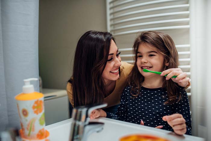 Mother helping child brush teeth