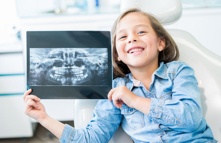 Girl at the dentist holding and x-ray and looking at the camera smiling