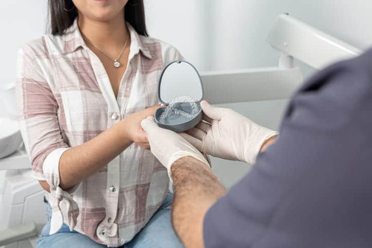 A dentist hands their patient a pair of Invisalign retainers.