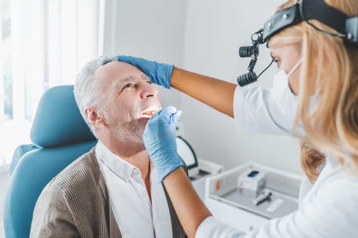 A dentist is examining a man's mouth.