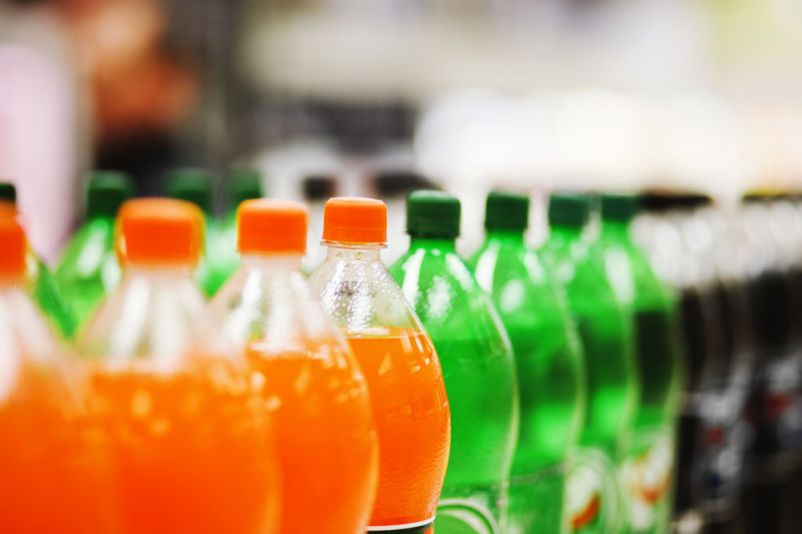 A long line of unbranded soda bottles in various flavours and colors, the focus on the center of the line.