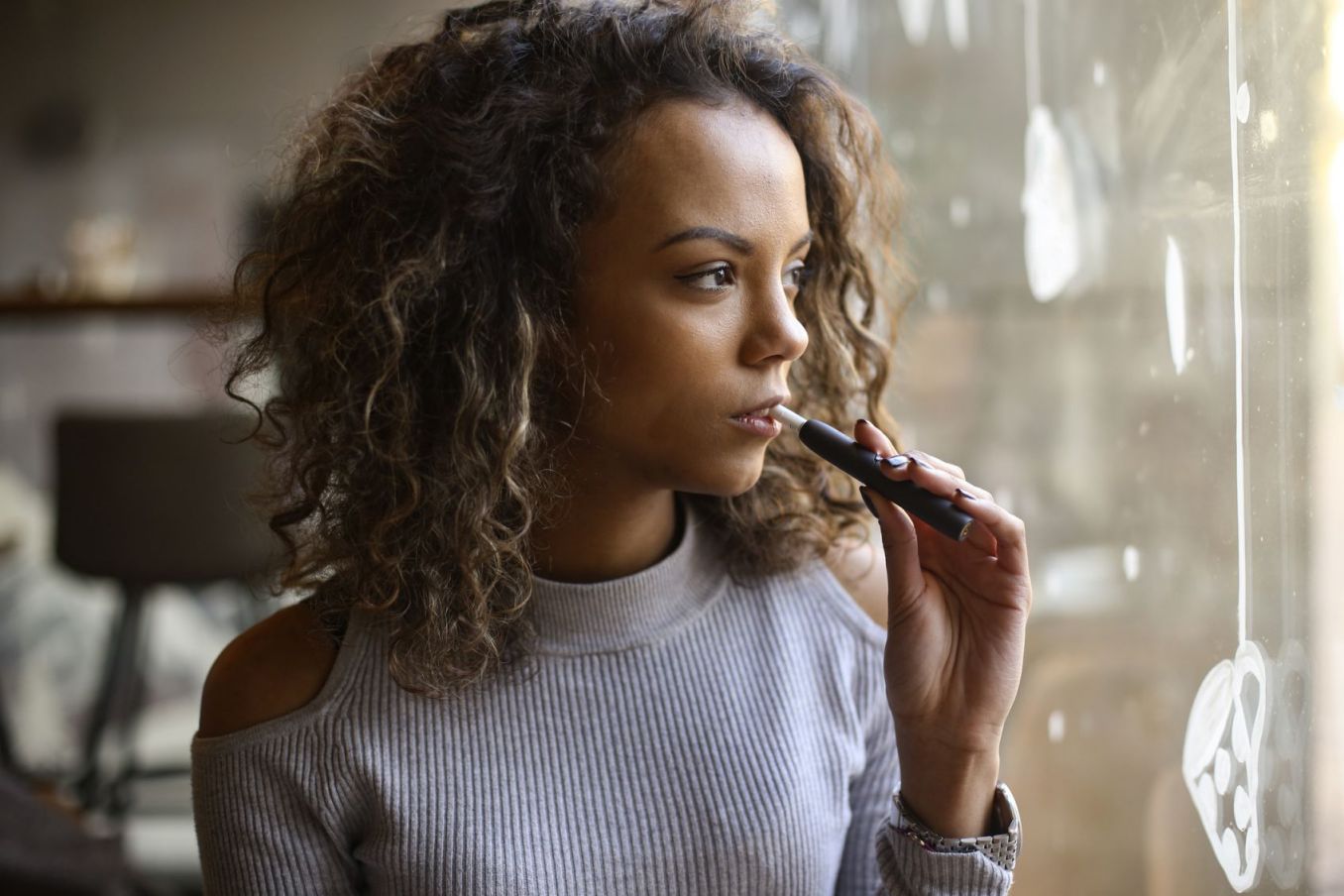 Young woman in a bar smoking an electronic cigarette. About 25 years old, Mixed race female.