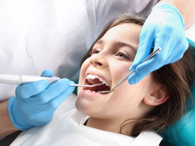 dentist performing a teeth cleaning for a young girl