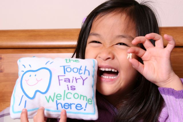 Little girl holding up tooth and tooth fairy pillow