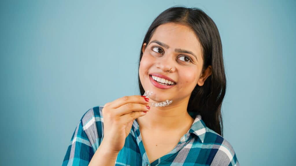 A woman smiling as she holds a clear aligner in her hand.