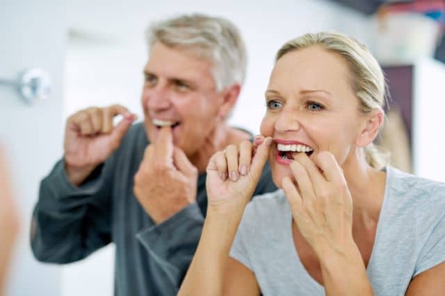 married couple flossing their teeth to maintain good oral health