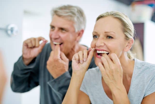 Married couple flossing their teeth to maintain good oral health