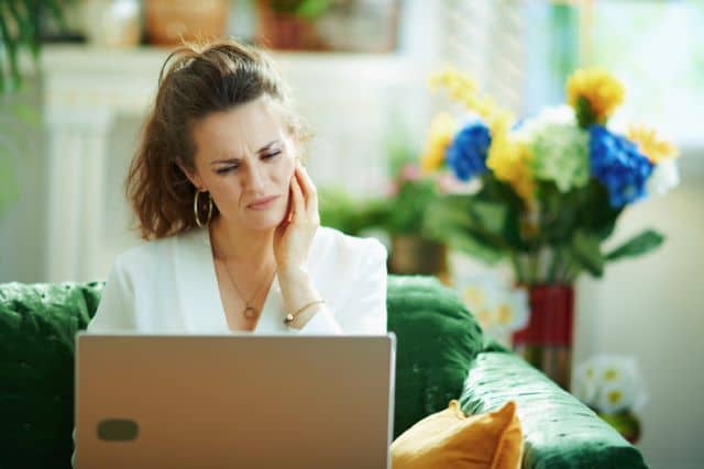 Woman with unbearable tooth pain scheduling an appointment online for an emergency dentist