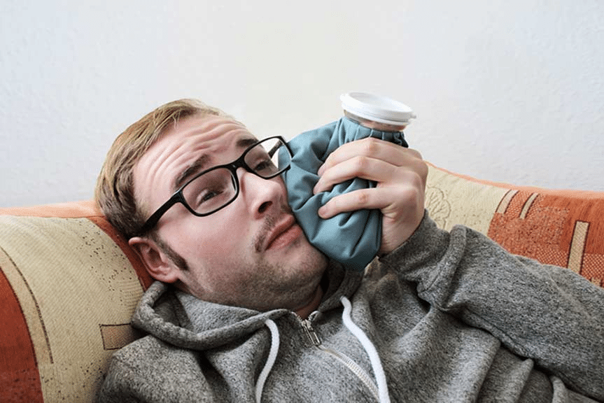 Young man lying on the couch with an icepack on his cheek.