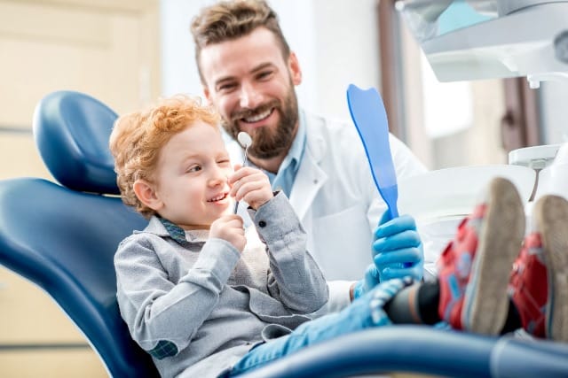 dentist with child looking into a small mirror with dentist tool