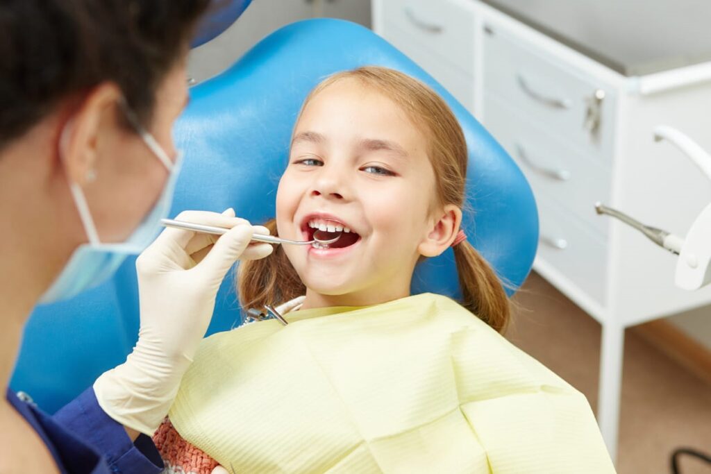 A little girl smiling as a pediatric dentist checks out her teeth in Las Vegas.