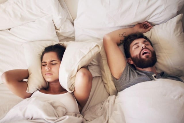women covering ears while her husband snores while they sleep in bed