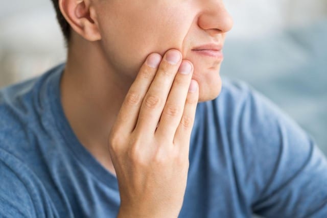 man with toothache holding the side of his cheek