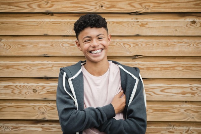 Teenager wearing braces in front of a wood wall