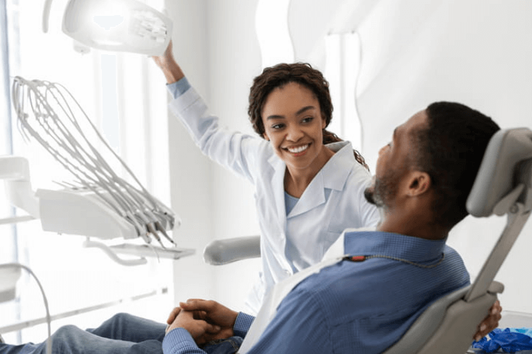 a female dentist is caring for her male patient as he sits in a dentist chair.