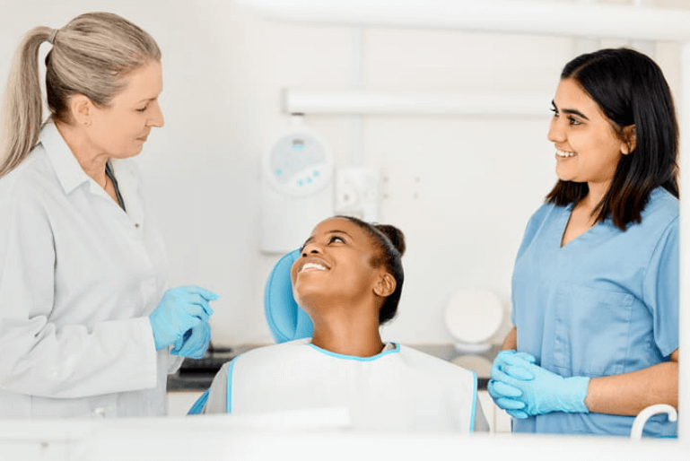 two female dentists are speaking with their female patient about dental bridges.