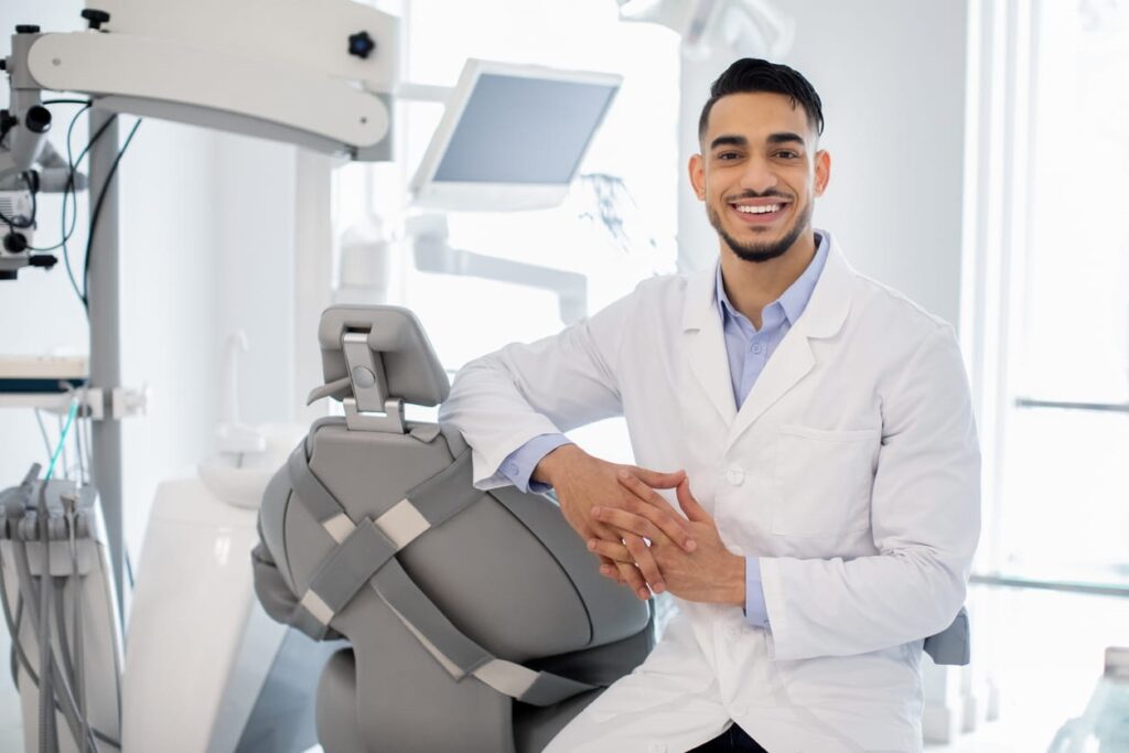 A general dentist smiling while leaning against an empty patient chair.
