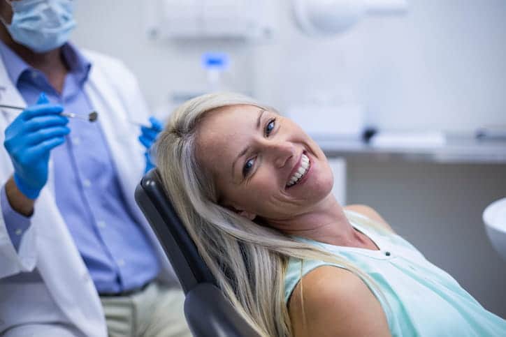 A woman smiling at the dentist's office, with the dentist in the background.