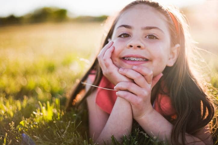 A little girl laying in the grass, smiling with metal braces.
