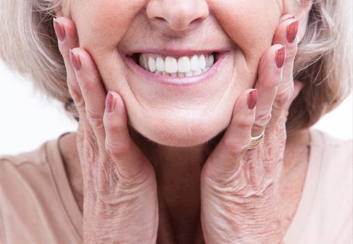 Focus is on an elderly woman smiling with permanent dentures.
