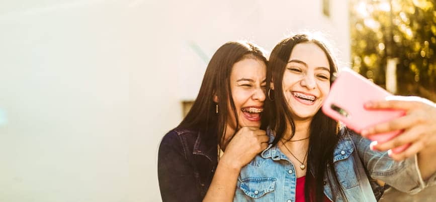 Two teenagers smiling with metal braces, taking a selfie.