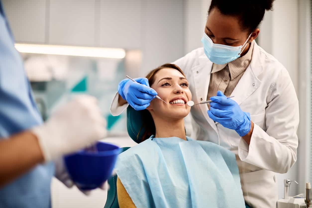 A dentist performing a dental cleaning on a patient who is smiling in the dental chair.