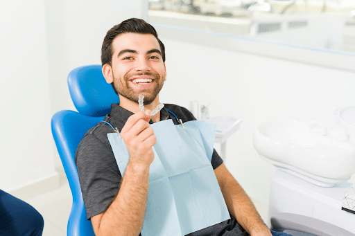A man smiling at the dentist office, holding a clear aligner.