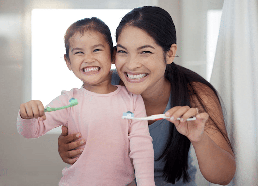 A mother and daughter smiling together while holding toothbrushes in Sparks, Nevada.