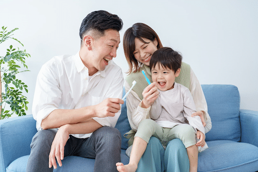 A mother and father sit on the couch with their child who's holding a toothbrush after seeing a pediatric dentist in Las Vegas.