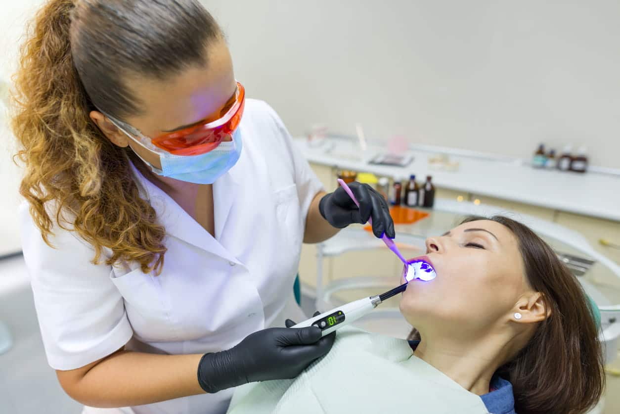 A patient is under sedation while at the dentist's office. The dentist is examining her teeth.