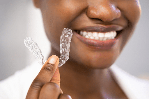 A smiling woman is holding up her clear aligner.