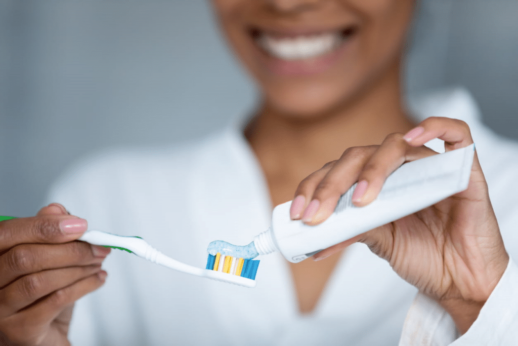A woman is smiling as she applies toothpaste to her toothbrush to help prevent gum disease.