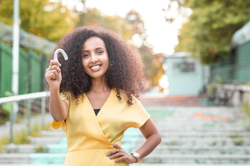 A woman smiling as she holds a clear aligner in her hand.