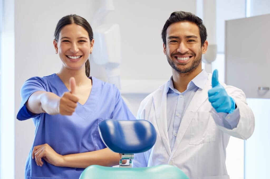 Two dental hygienists smiling and giving a thumbs up.