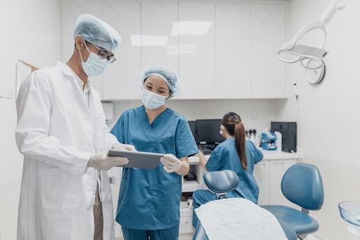 Two general dentists examining a patient's chart as an assistant prepares the room.