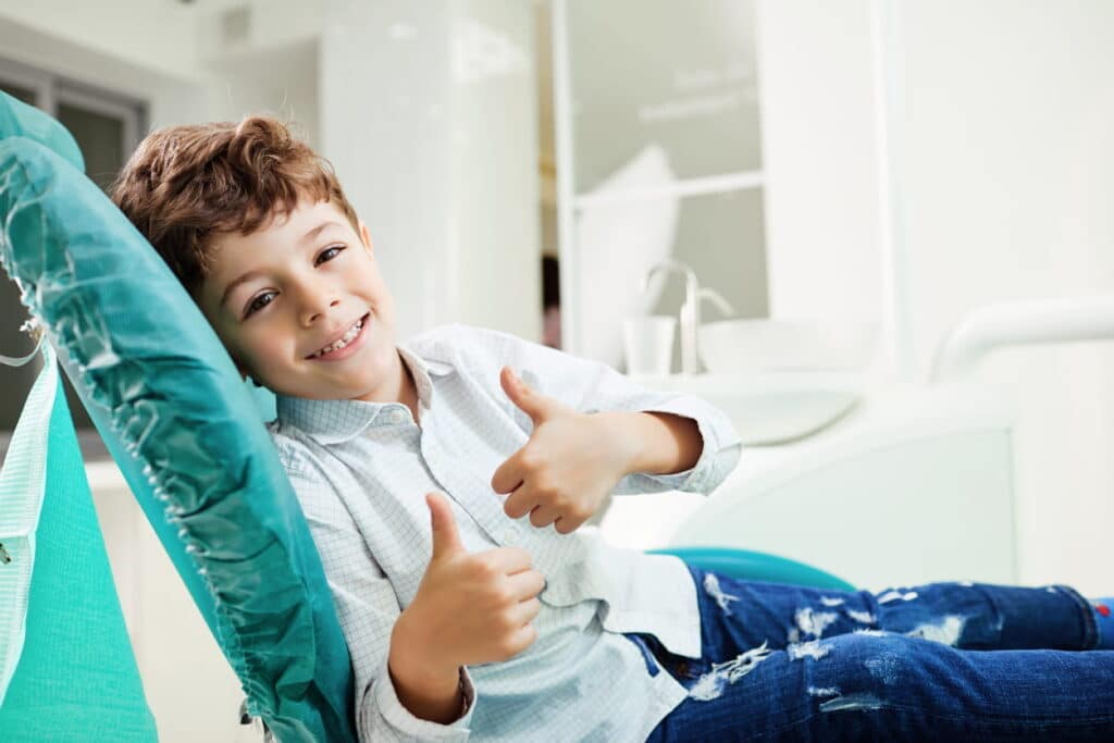 A boy smiling and giving two thumbs up while lying in a dentist chair in Las Vegas. 