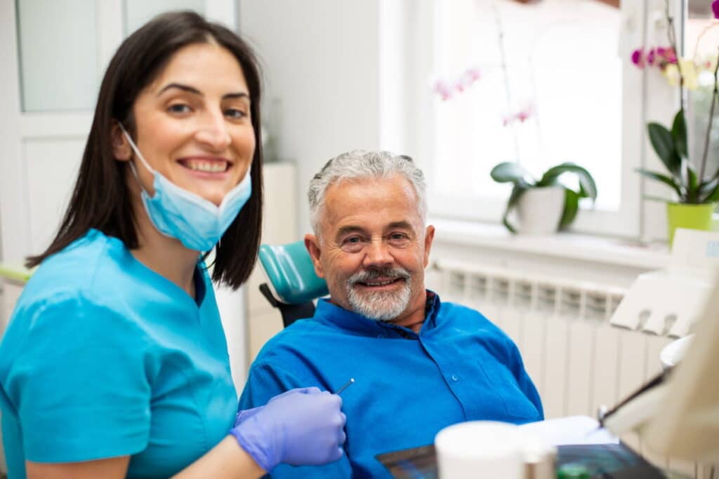 A dentist in North Las Vegas with her medical mask pulled down and her patient in a chair both smiling.