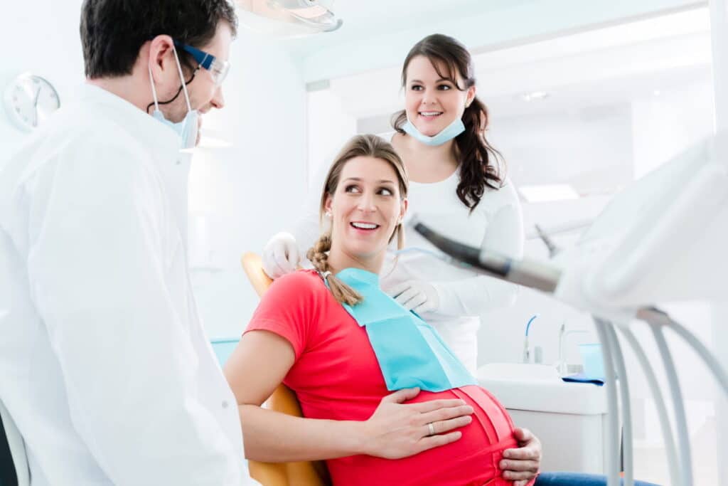 A pregnant woman at the dentists, smiling and chatting with them.