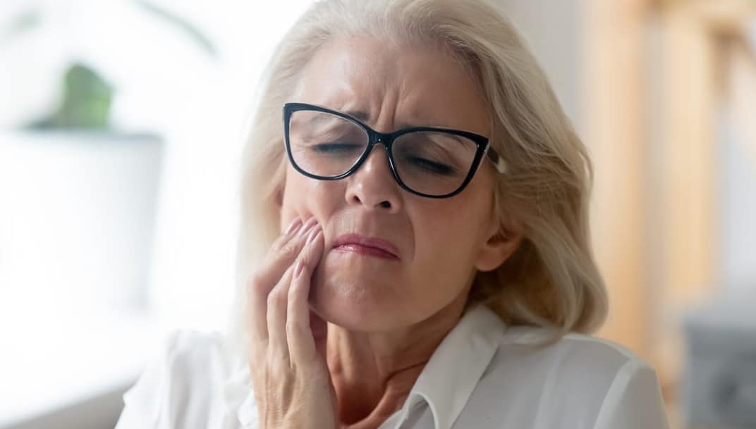 A woman holding her jaw in pain from an infected tooth prior to a root canal.