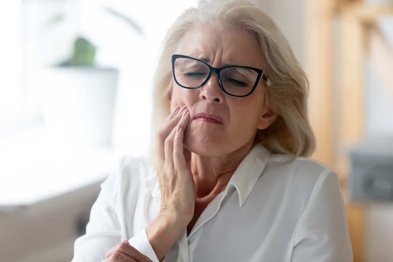 A woman holding her jaw in pain from an infected tooth prior to a root canal.
